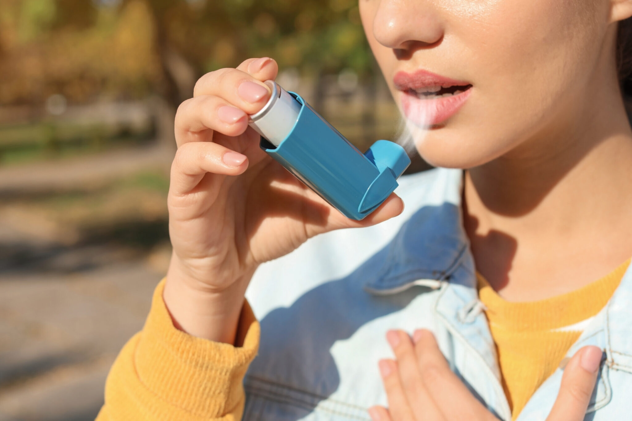Woman using asthma inhaler outdoors. Health care